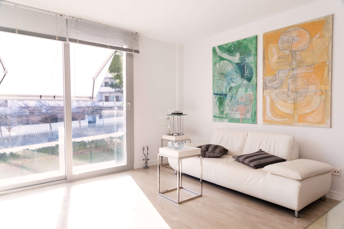 Salon lumineux avec canapé en cuir blanc, deux grands tableaux abstraits et baies vitrées toute hauteur.