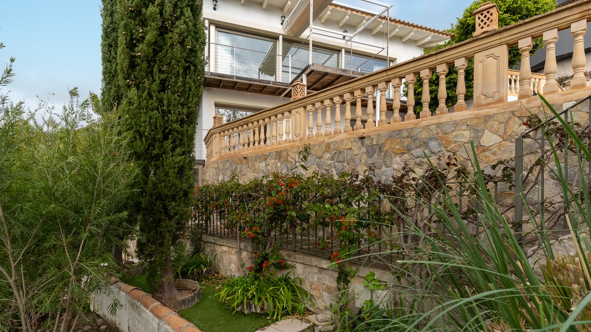 Jardin en terrasses avec murs en pierre, balustrades classiques et cyprès devant une villa blanche.