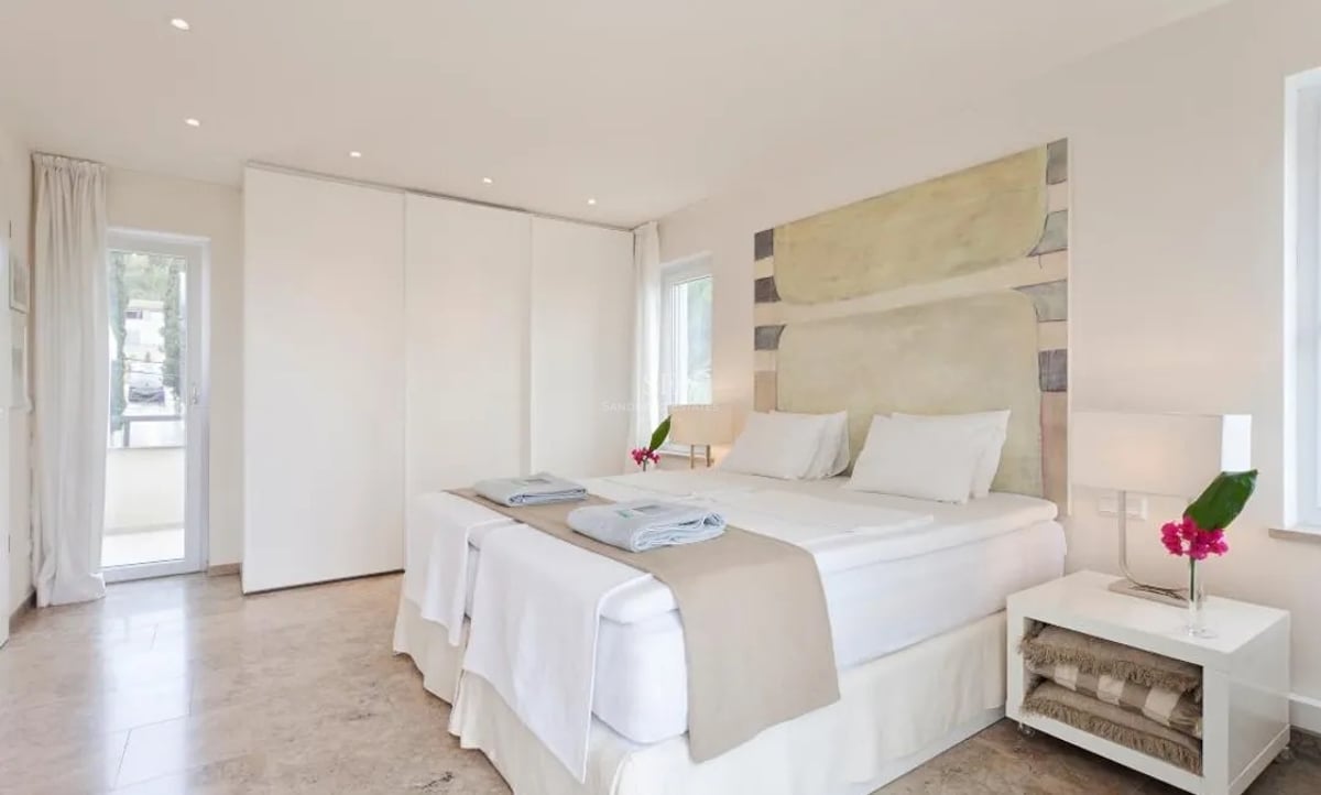 Chambre spacieuse blanche avec sol en marbre, placards intégrés et accès direct à la terrasse.