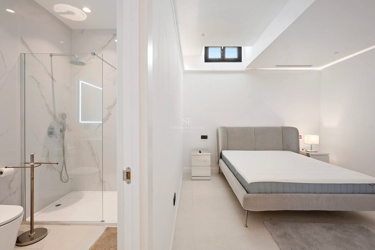 Chambre moderne avec lit gris et porte ouverte sur une douche à l'italienne en marbre.