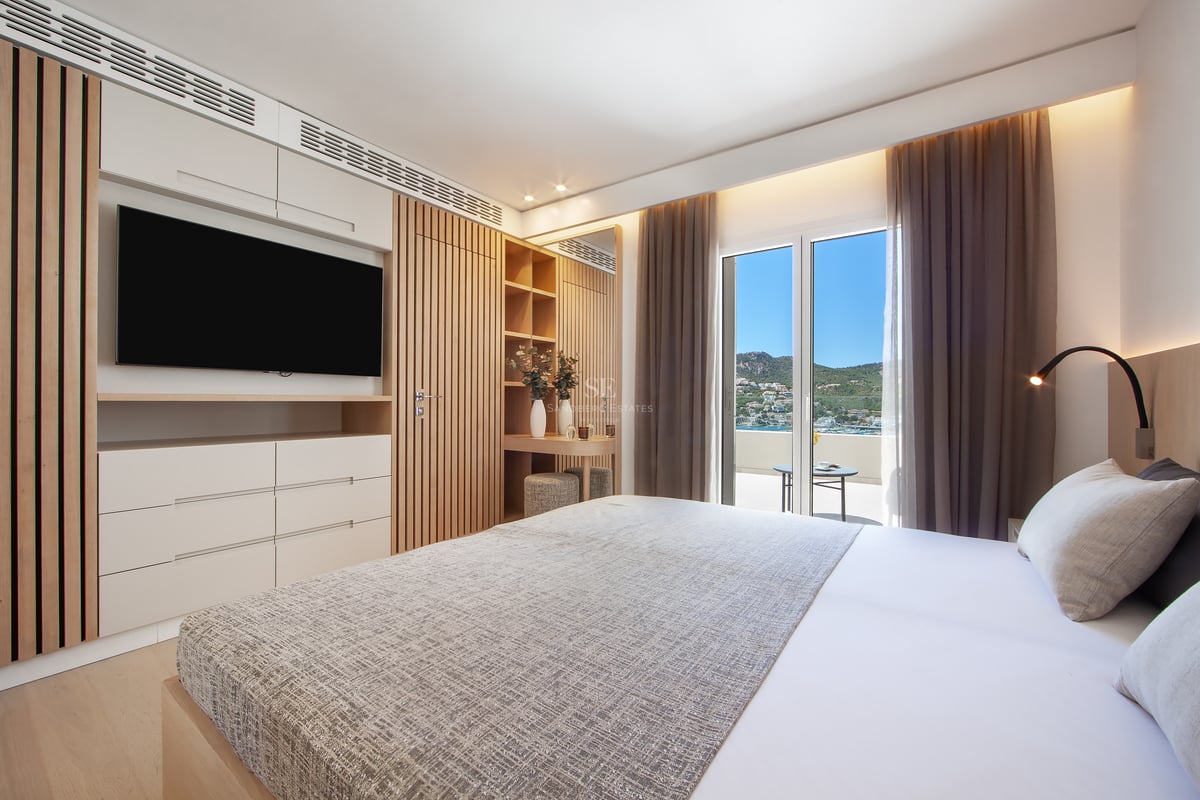 Chambre lumineuse avec grand lit, boiseries, TV et balcon offrant une vue sur la côte et les montagnes.