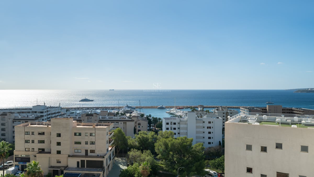 Vue en hauteur d'une ville côtière, d'un port rempli de yachts et de la mer Méditerranée sous un ciel bleu.