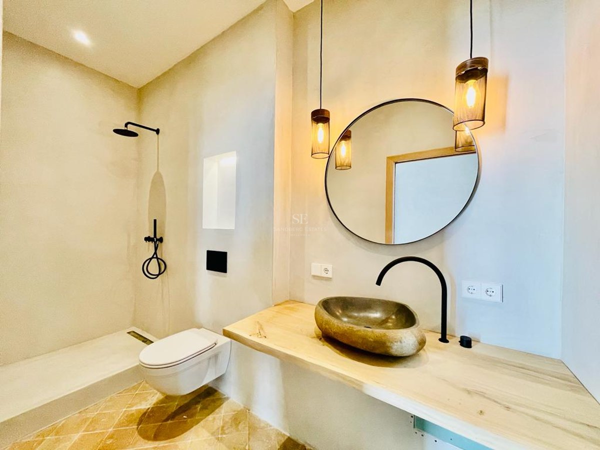 Salle de bains moderne avec vasque en pierre sur plan en bois, miroir circulaire et robinetterie noire mate.