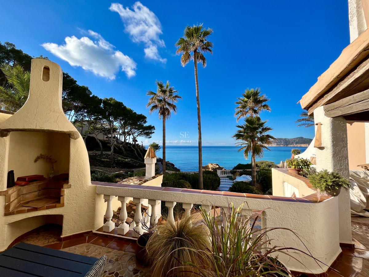 Terrasse avec cheminée extérieure blanche et balustrade offrant une vue sur des palmiers et la mer bleue.