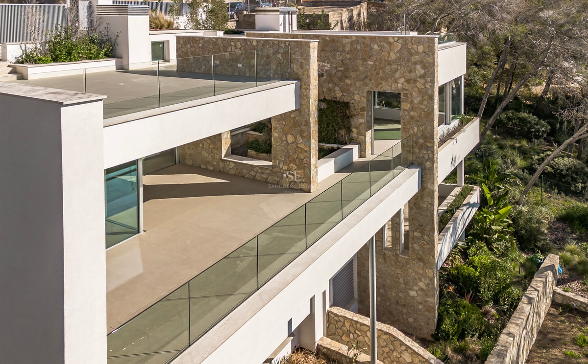 Villa contemporaine à plusieurs étages avec murs en pierre naturelle, garde-corps en verre et vastes terrasses.