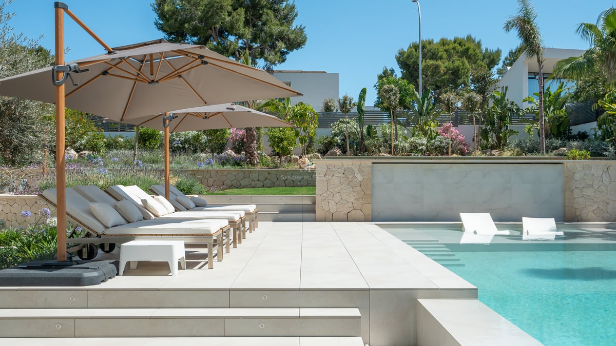 Piscine contemporaine avec chaises longues immergées et terrasse ombragée par des parasols.