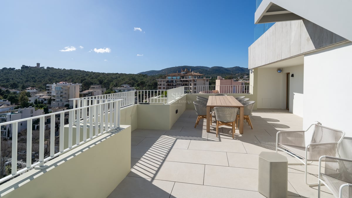 Terrasse moderne spacieuse avec table à manger en bois, chaises tressées et vue sur les collines environnantes.