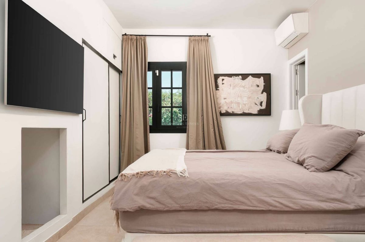 Chambre lumineuse avec lit mauve, TV murale, rangements intégrés et fenêtre avec rideaux taupe.