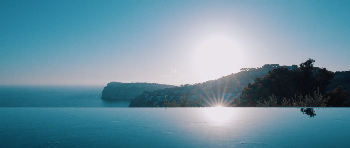 Littoral et collines se reflétant dans une piscine à débordement lors d'un coucher de soleil sur la Méditerranée.