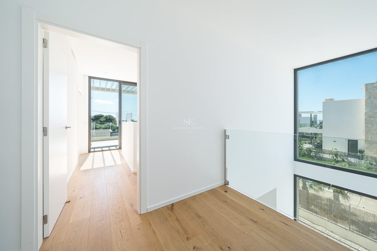 Couloir lumineux avec parquet clair, rampe en verre et grandes fenêtres offrant une vue sur l'extérieur.