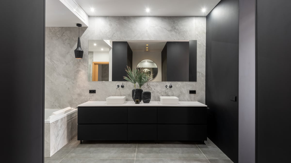 Salle de bains de luxe avec murs en marbre, double vasque blanche sur meuble noir et grand miroir.