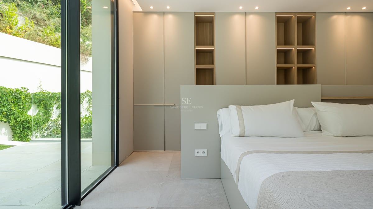 Chambre contemporaine avec baies vitrées, placards toute hauteur et étagères en bois avec éclairage LED.