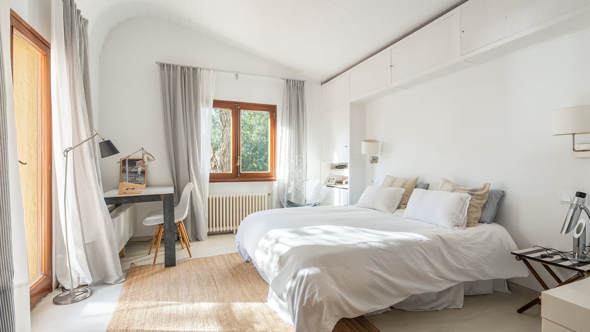 Chambre baignée de lumière avec literie blanche, plafond voûté, tapis en fibres naturelles et bureau d'angle.