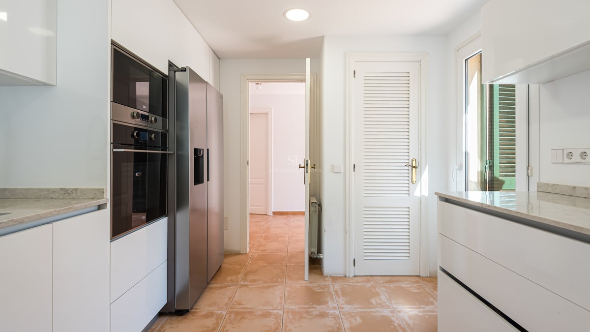 Cuisine lumineuse avec placards blancs, plans de travail en marbre, frigo inox et sol en terre cuite.