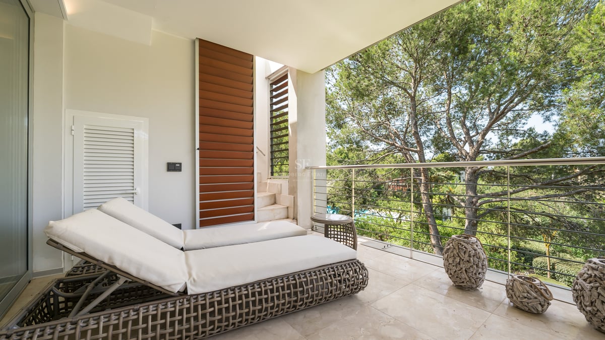 Terrasse moderne avec bains de soleil, sol en marbre et garde-corps en inox donnant sur une pinède.