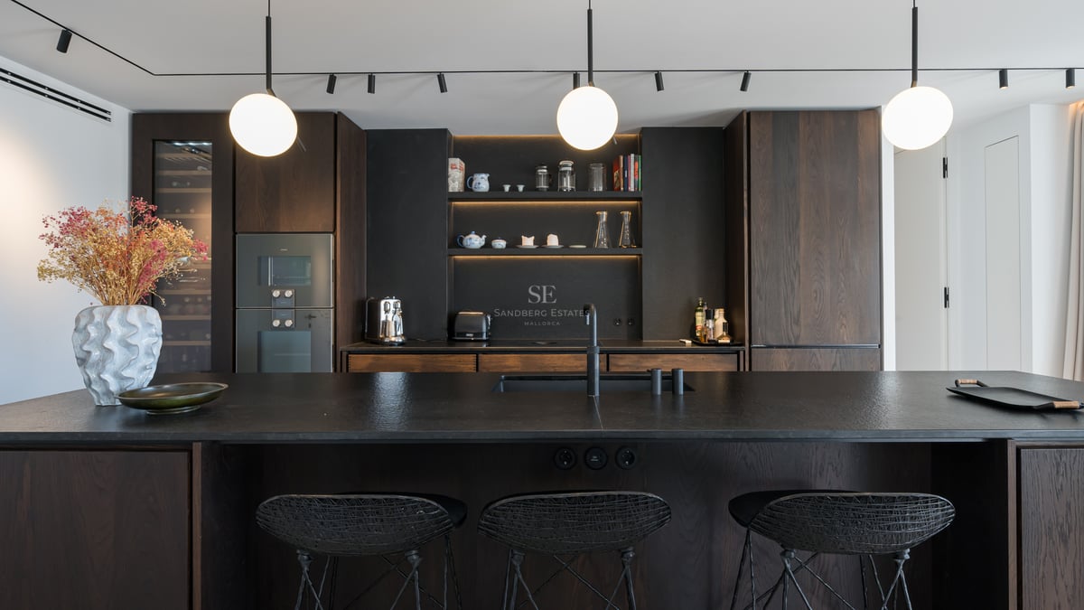 Cuisine moderne avec placards en bois sombre, îlot noir texturé avec tabourets et suspensions sphériques.