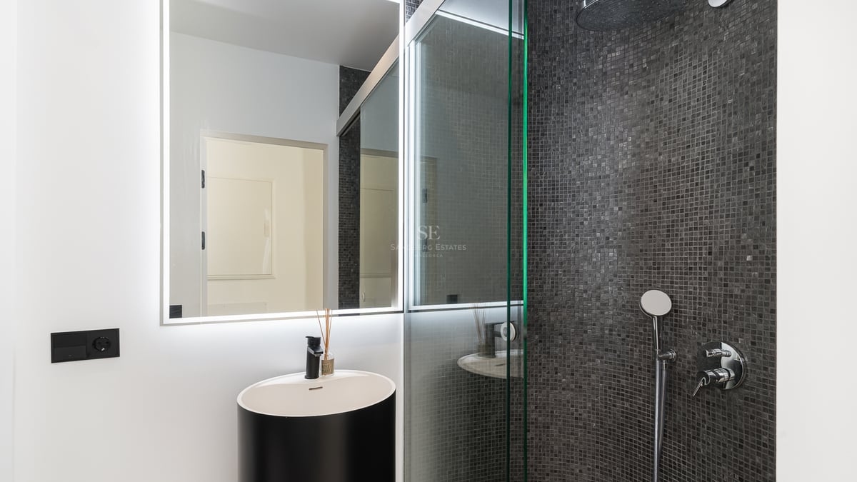 Salle de bain contemporaine avec vasque cylindrique noire, miroir rétroéclairé LED et douche en mosaïque anthracite.