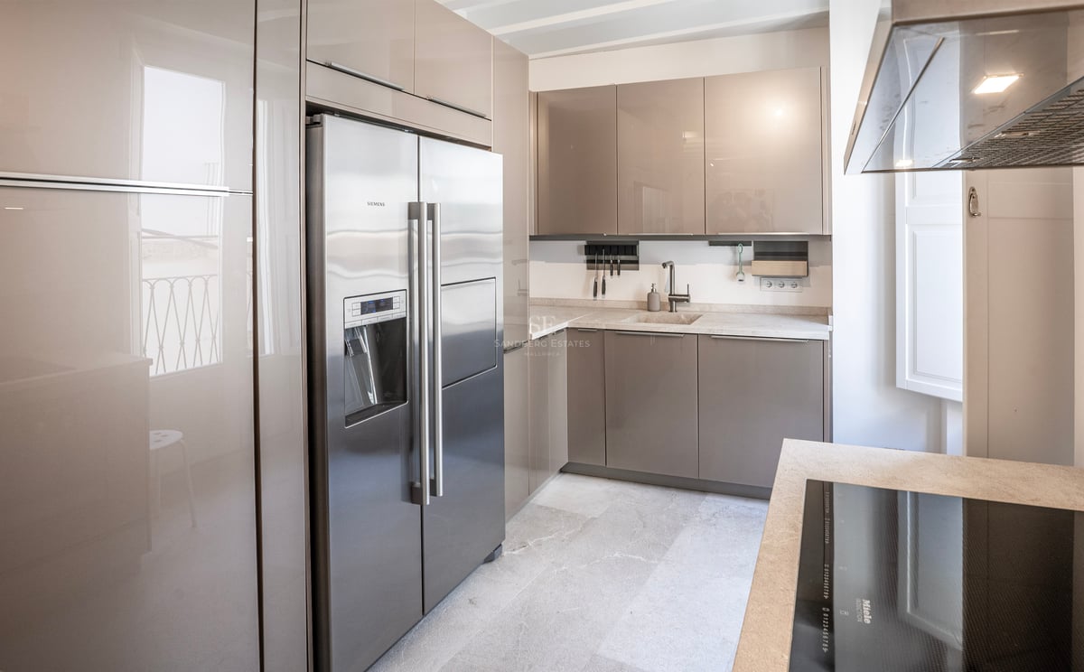 Cuisine moderne avec placards taupe brillant, réfrigérateur en acier inoxydable et plans de travail en pierre claire.