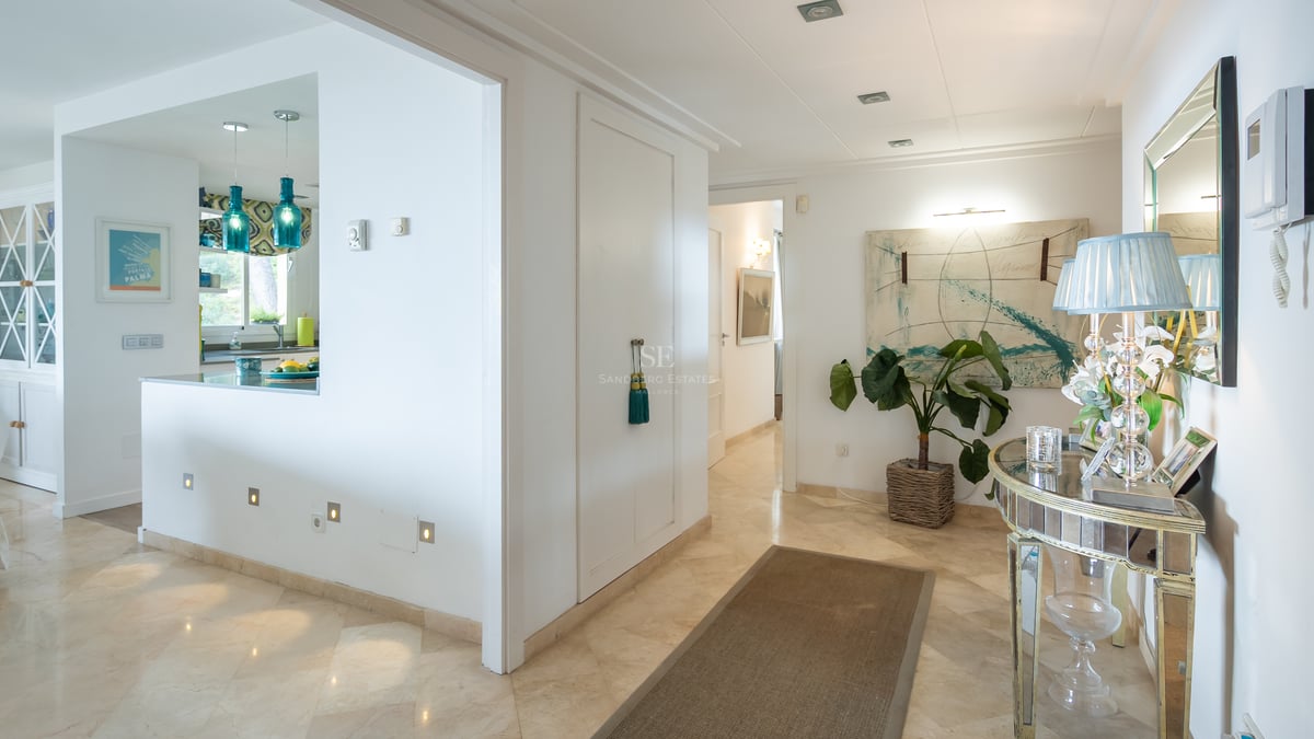 Entrée lumineuse avec sol en marbre crème, console miroir et suspensions turquoise ouvrant sur la cuisine.