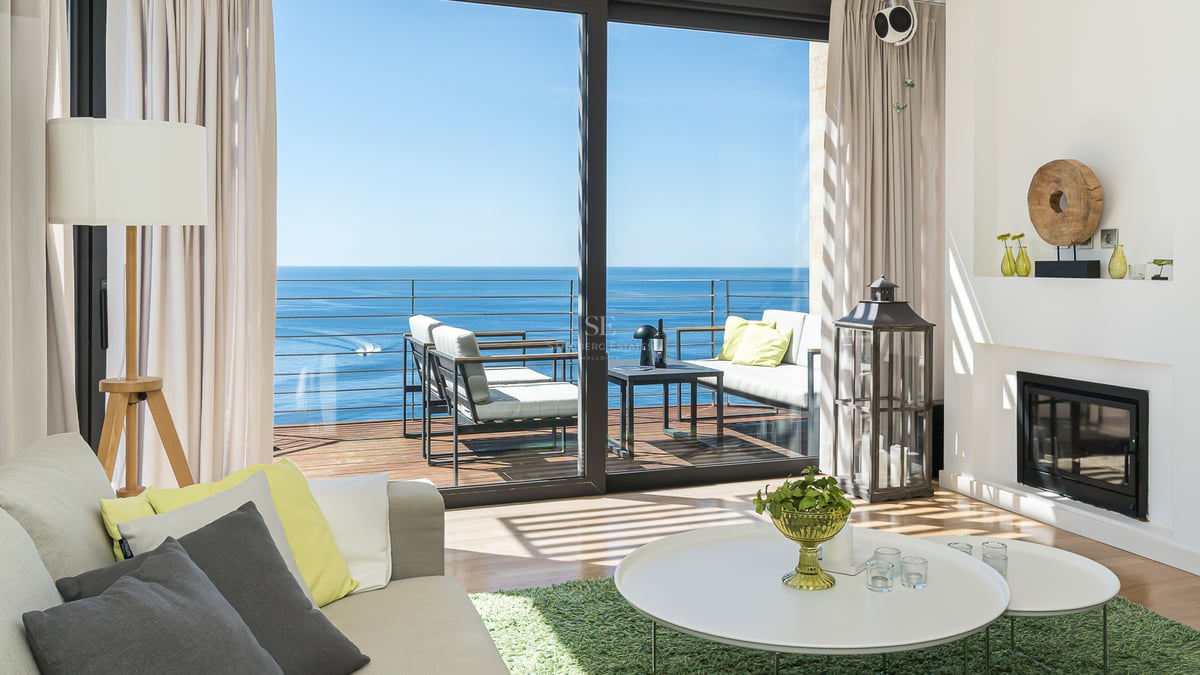 Salon moderne avec cheminée et baies vitrées ouvrant sur une terrasse avec vue directe sur la mer Méditerranée.