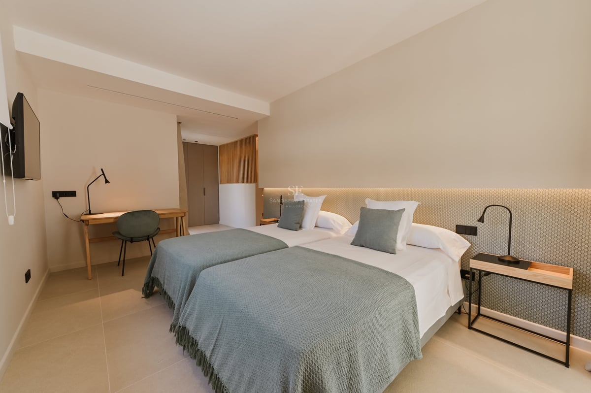Chambre moderne avec lits jumeaux, jetés vert sauge, bureau en bois et éclairage chaleureux indirect.