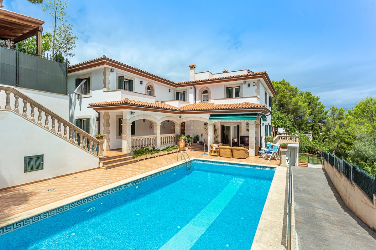 Grande piscine rectangulaire devant une villa méditerranéenne blanche à deux étages avec toit en terre cuite.