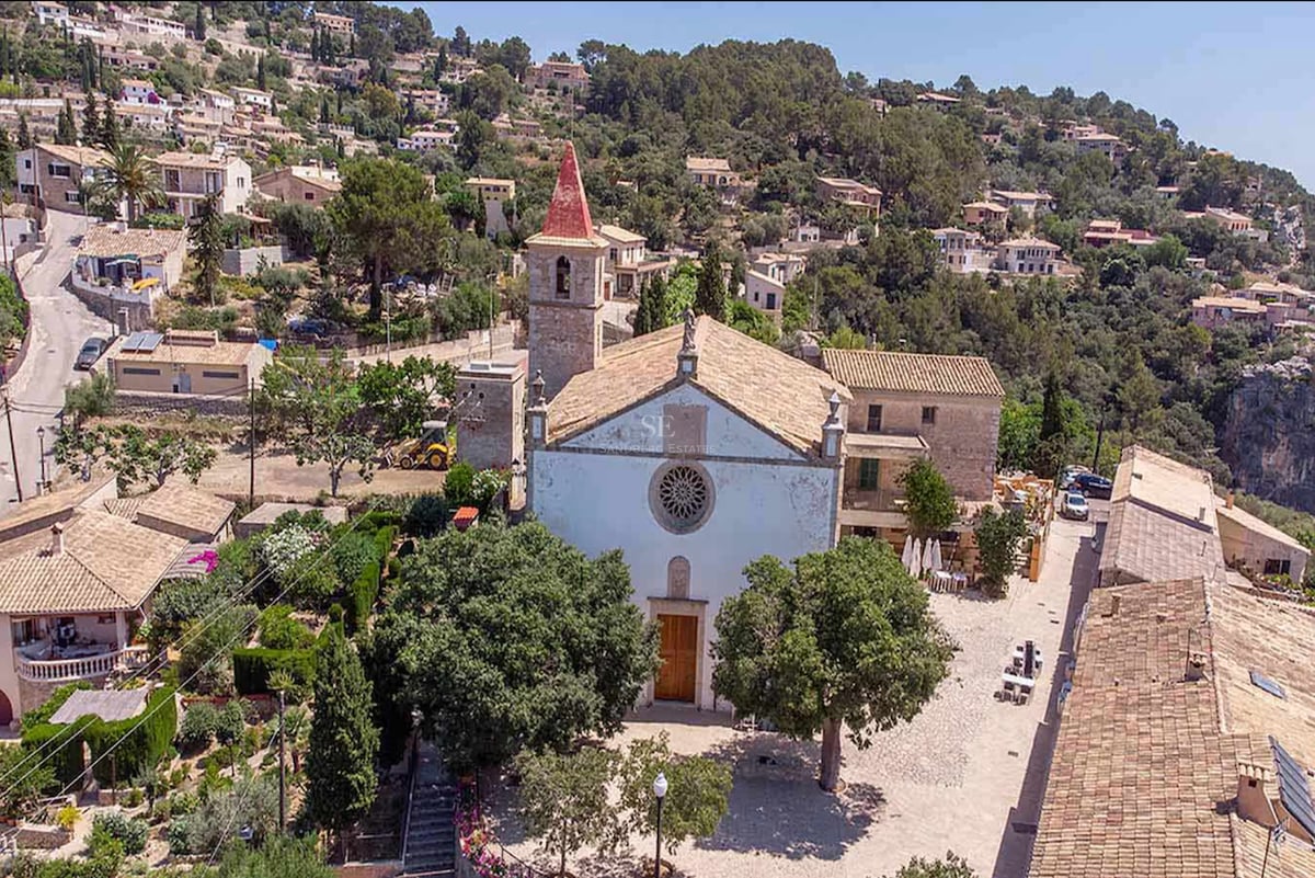 Vue aérienne d'une église traditionnelle en pierre et de maisons méditerranéennes dans un village à flanc de colline.