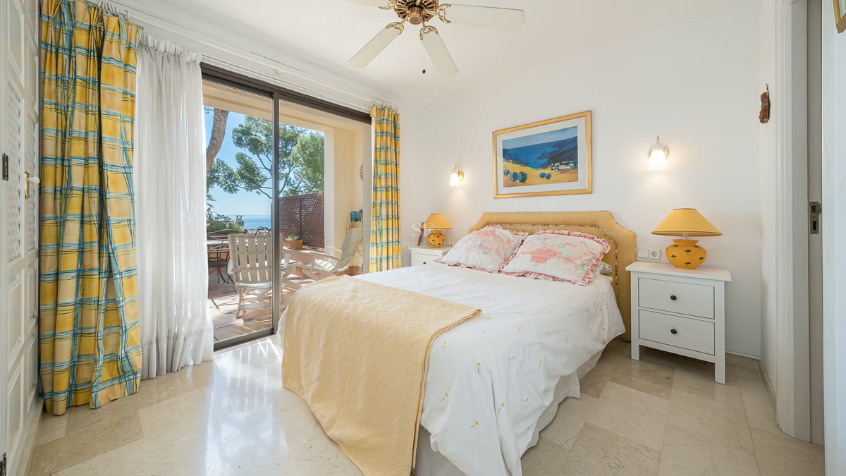 Chambre lumineuse avec sol en marbre, décor jaune et portes coulissantes ouvrant sur une terrasse avec vue sur la mer.
