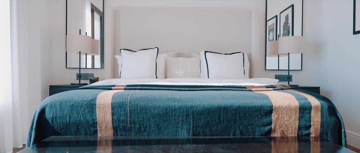 Lit king-size avec jeté de lit bleu canard, lampes design symétriques et miroirs muraux dans une suite de luxe.