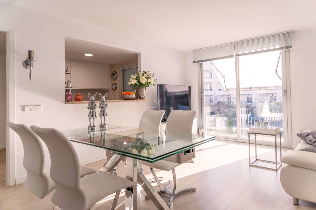 Espace salle à manger contemporain avec table en verre, chaises en cuir blanc et grandes baies vitrées.