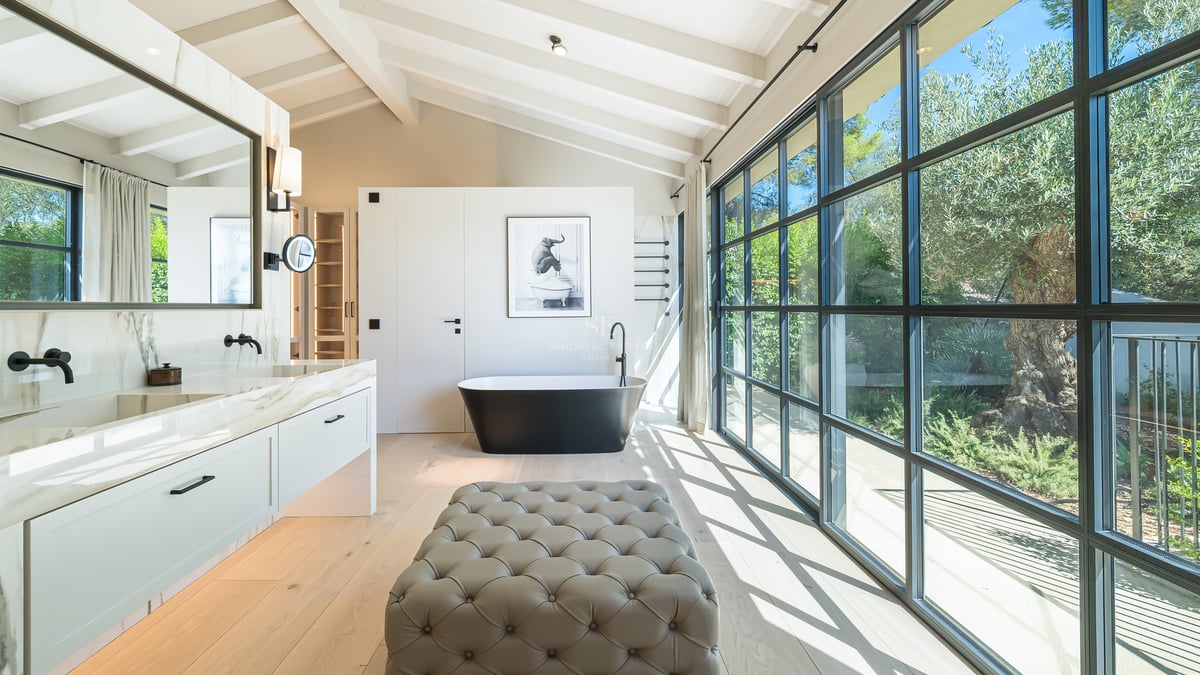Salle de bains de luxe avec baignoire îlot noire, double vasque en marbre et grandes baies vitrées donnant sur un jardin.