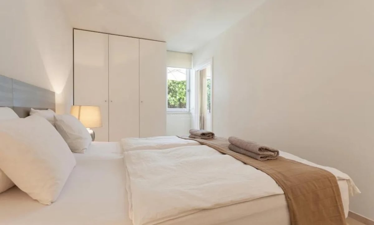 Chambre blanche lumineuse avec lits jumeaux, placards intégrés et vue sur la verdure.