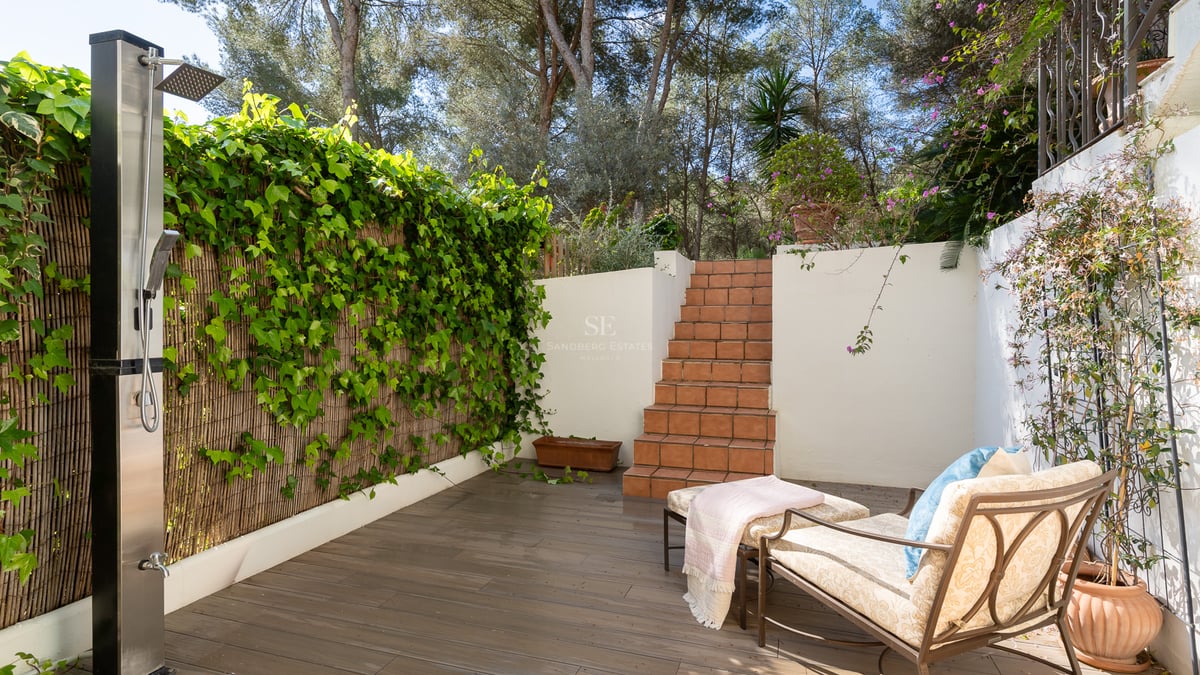 Terrasse extérieure avec douche moderne en inox, marches en terre cuite, chaise longue et mur de lierre vert.