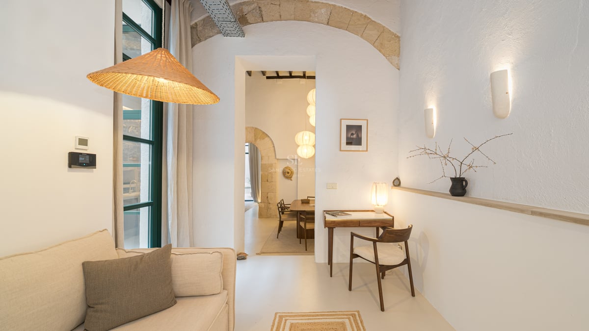 Salon blanc avec arches en pierre, suspension en osier, canapé et petit bureau en bois avec chaise.