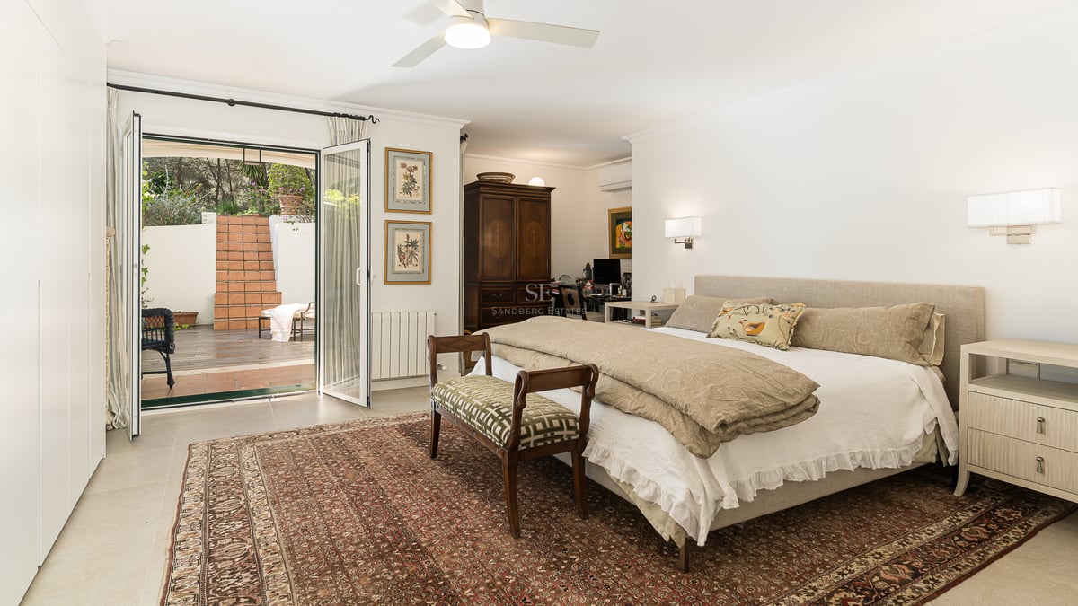 Grande chambre principale avec lit, tapis oriental et portes vitrées ouvrant sur un patio en terre cuite.