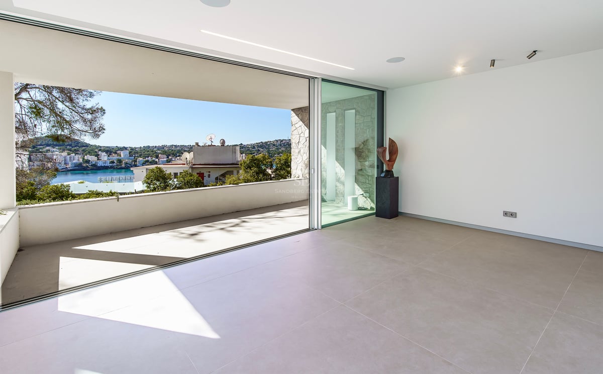 Intérieur minimaliste avec de grandes baies vitrées ouvrant sur une terrasse dominant la côte et la mer.