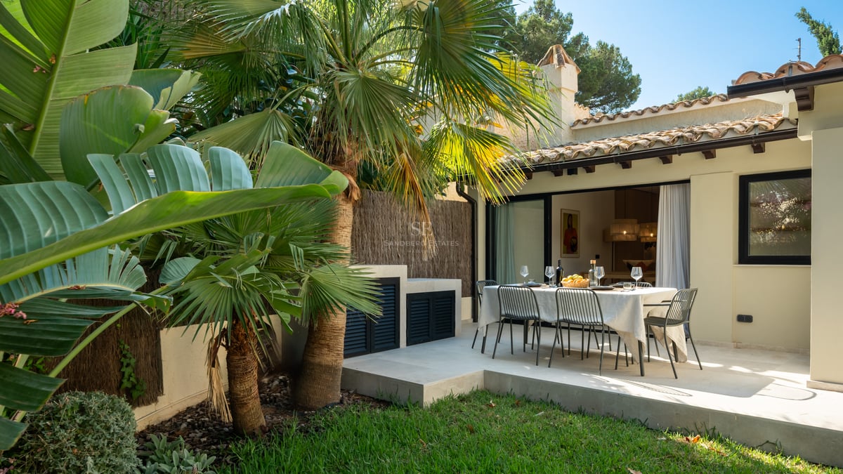 Table à manger extérieure sur une terrasse en pierre blanche entourée de palmiers et d'une façade de villa.