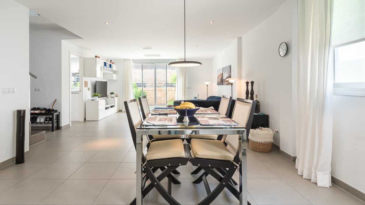 Table à manger moderne avec six chaises dans une pièce lumineuse à aire ouverte avec de grands carreaux au sol.