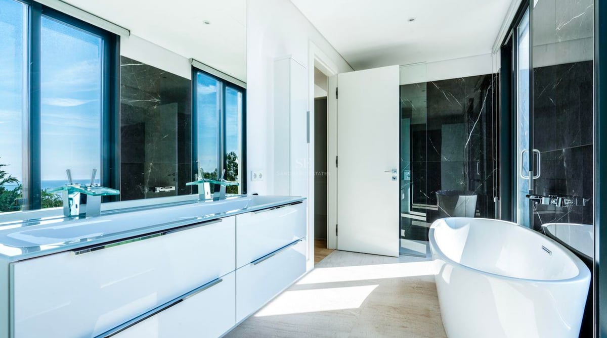 Salle de bain moderne avec baignoire îlot blanche, double vasque et mur en marbre noir avec vue sur la mer.