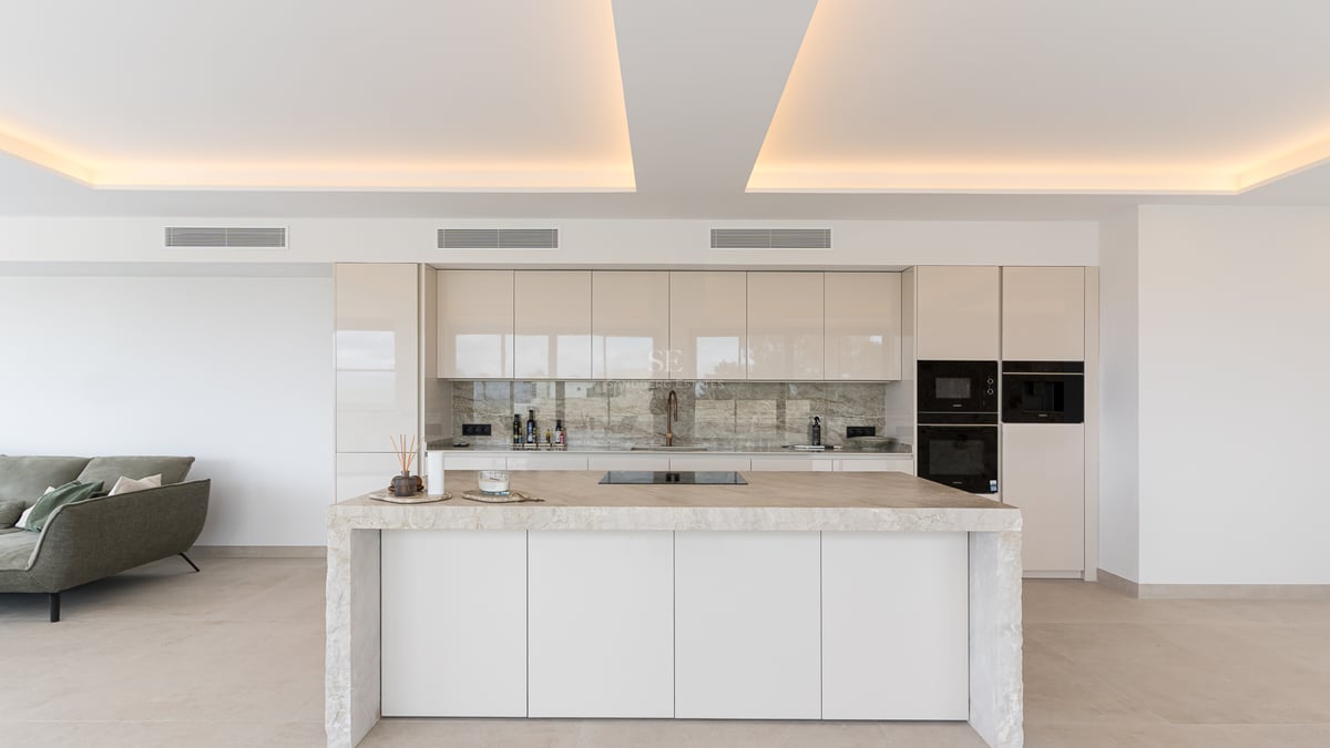 Cuisine minimaliste blanche avec îlot central en marbre et éclairage de plafond indirect dans une villa de luxe.