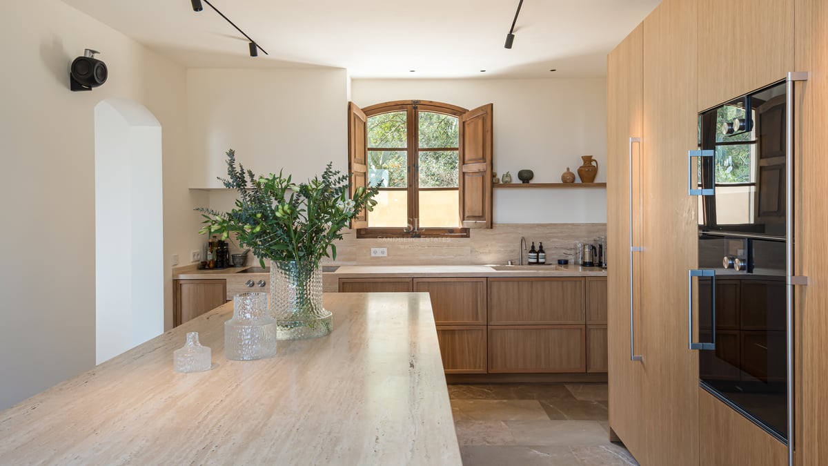 Cuisine minimaliste avec placards en chêne clair, îlot en travertin et volets en bois traditionnels.