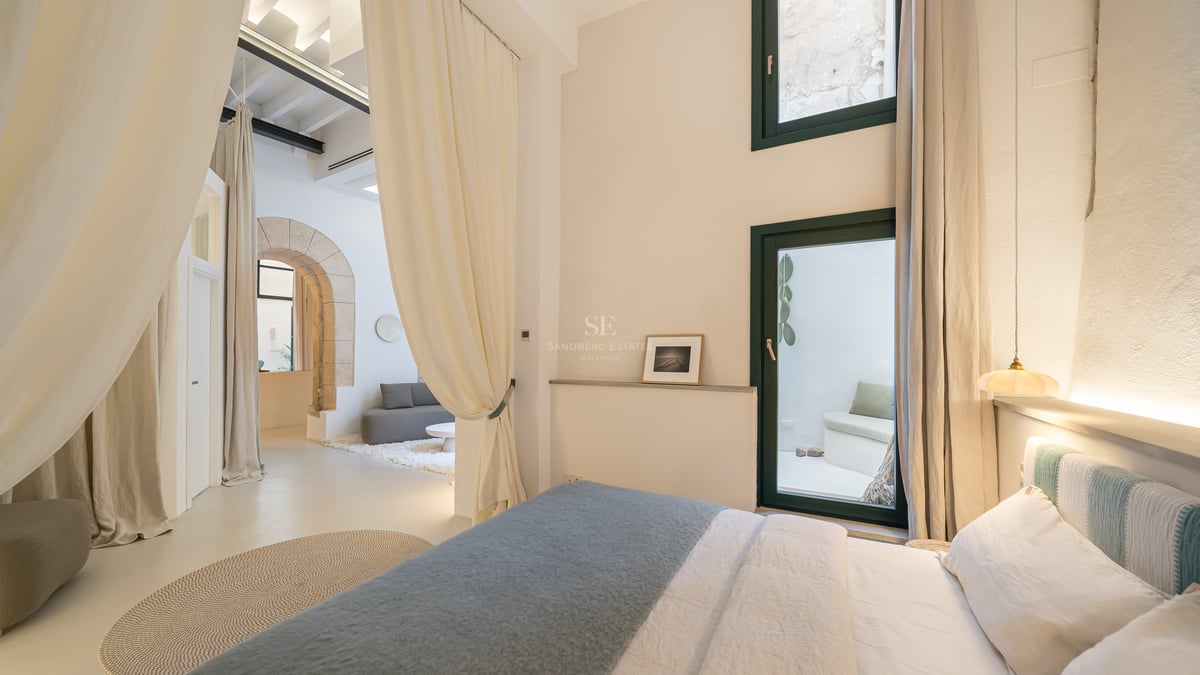 Chambre contemporaine avec une arche en pierre, de hauts plafonds, de grands rideaux crème et une décoration minimaliste.