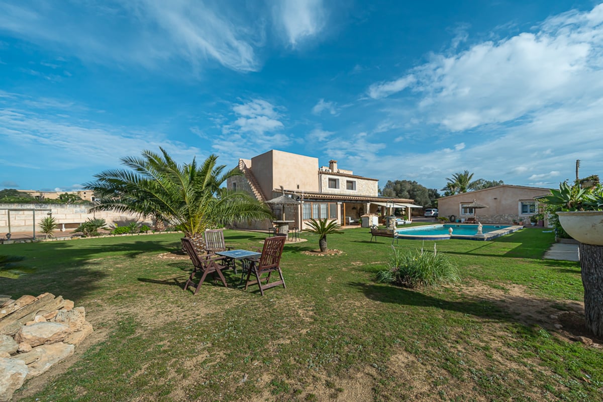 Exteriör av en rustik villa med stor gräsmatta, palmer, privat pool och utemöbler.