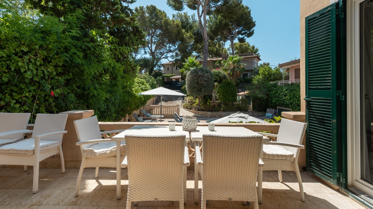 Salon de jardin en osier blanc sur une terrasse dallée de pierre surplombant un jardin méditerranéen et la piscine.