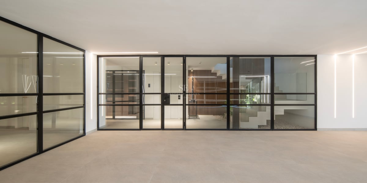 Entrée moderne avec parois vitrées à cadres noirs, carrelage beige et bandes lumineuses LED verticales.