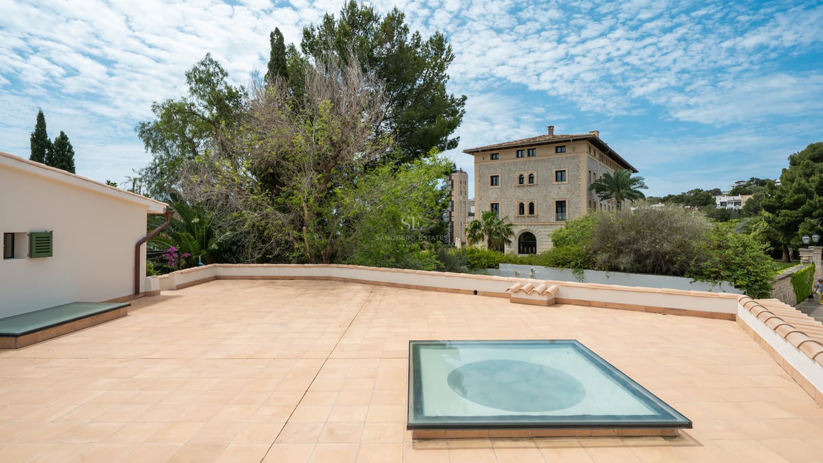 Grande terrasse sur le toit en terre cuite avec puits de lumière en verre, vue sur les pins et un manoir classique.