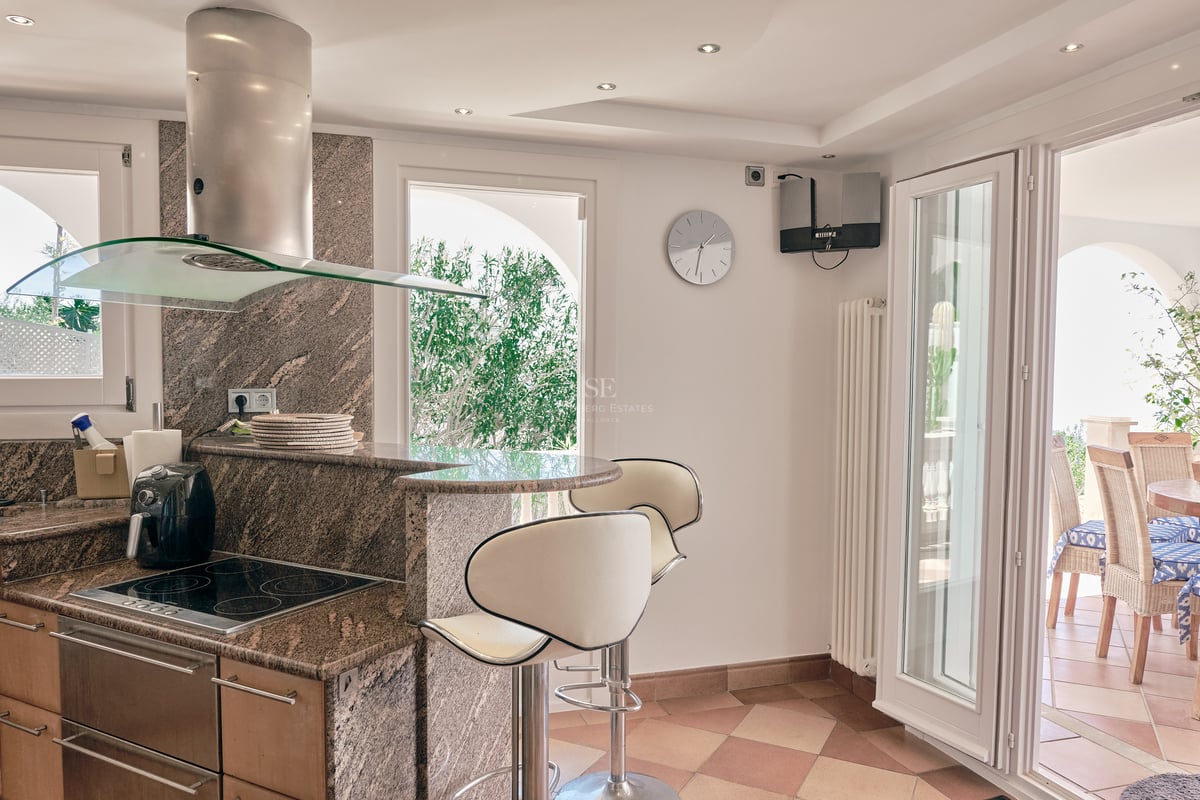 Cuisine moderne avec plans de travail en granit, bar et porte s'ouvrant sur une terrasse ombragée.