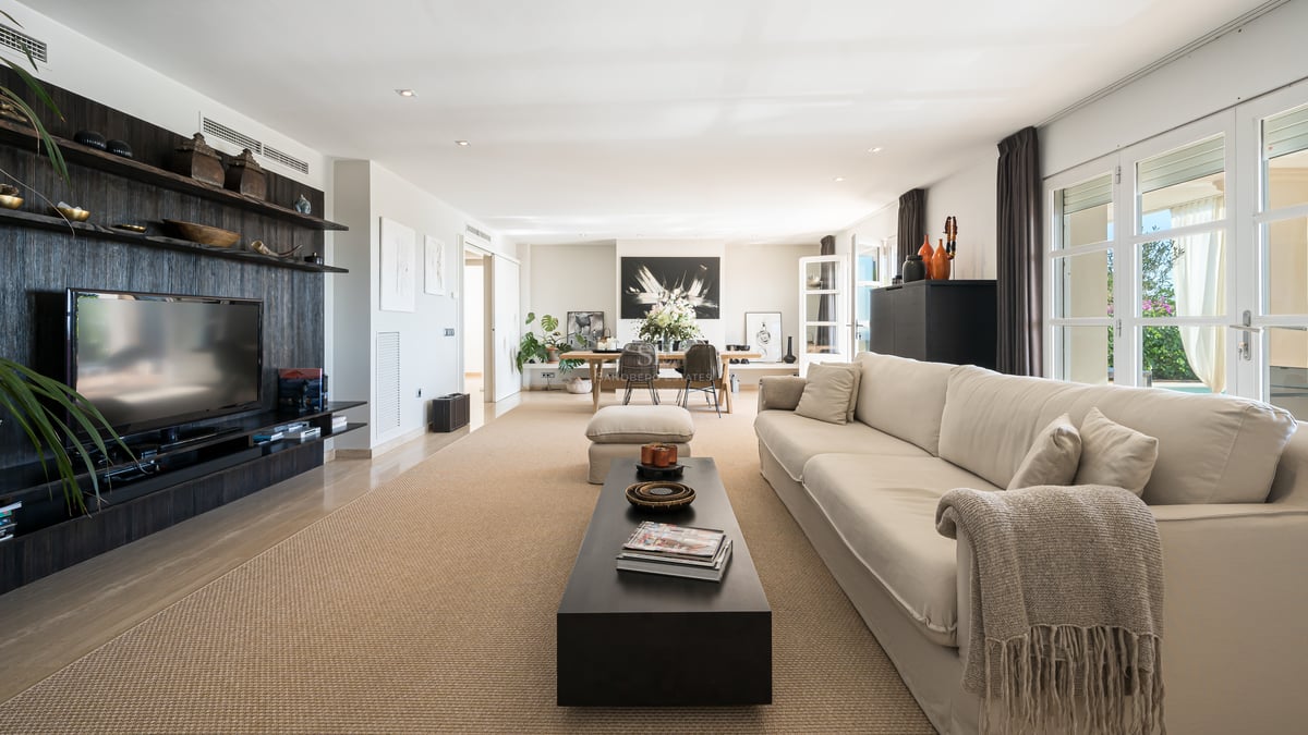 Vaste salon avec canapé beige, meuble multimédia en bois sombre, tapis en fibres naturelles et baies vitrées.