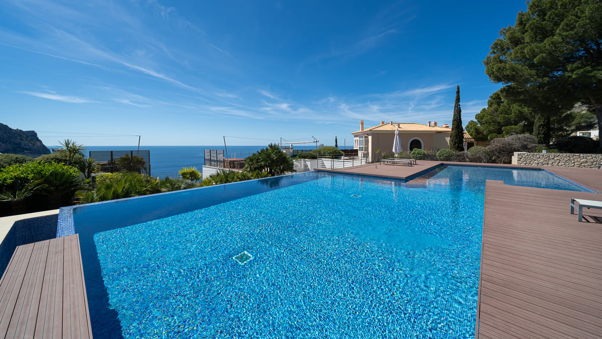 Grande piscine à débordement en mosaïque bleue donnant sur l'horizon marin avec terrasse en pierre.