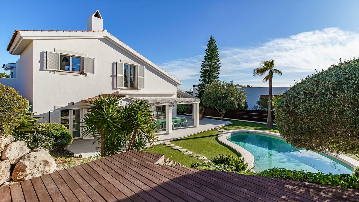 Villa blanche à deux étages avec une piscine en forme de haricot, une terrasse en bois et un jardin arboré.